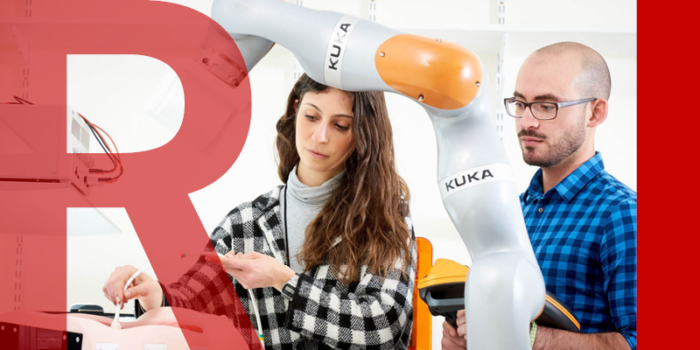 Two researchers testing a colonoscopy robot - a large metal arm reaching over a medical dummy body
