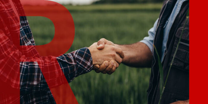 Two people shaking hands in front of a green field.