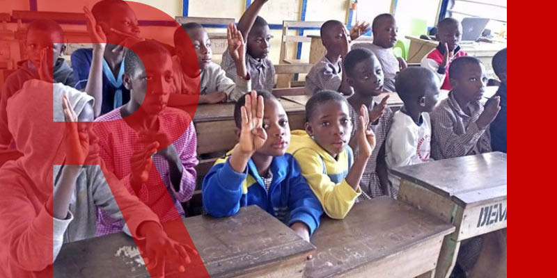 A full school classroom in Ghana, some children with their hands in the air