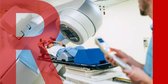 A patient undergoing radiotherapy. In the foreground, a radiologist holds a remote control for the linear accelerator machine.