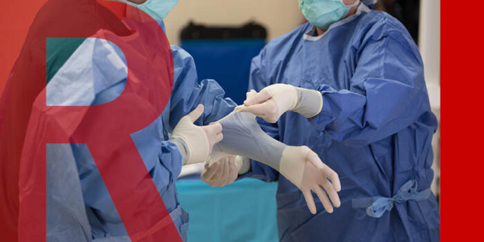 Two doctors wearing scrubs, pulling up the gloves of one of their arms.