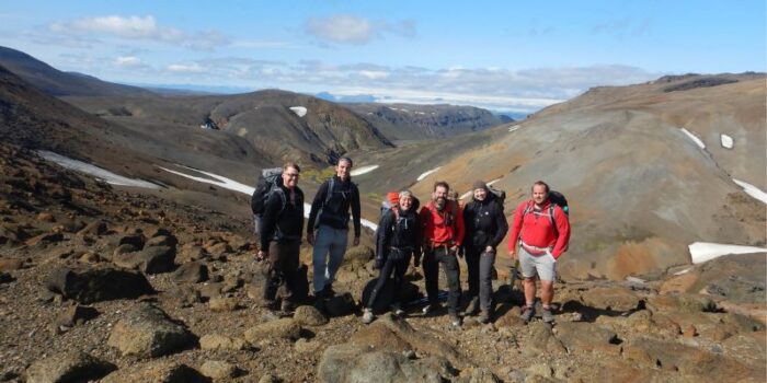 A group of people wearing hiking gear, standing on a rocky valley in front of a mountain range in Iceland