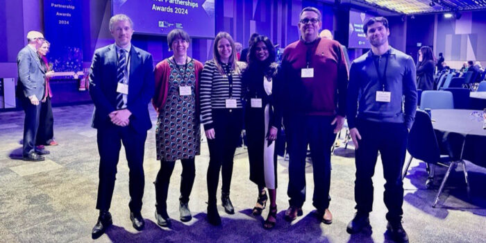 A group of people wearing smart clothes at a conference, standing together and smiling at the camera