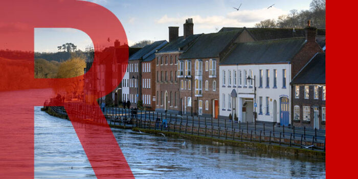 A row of houses close to a river which has flood defences along its banks