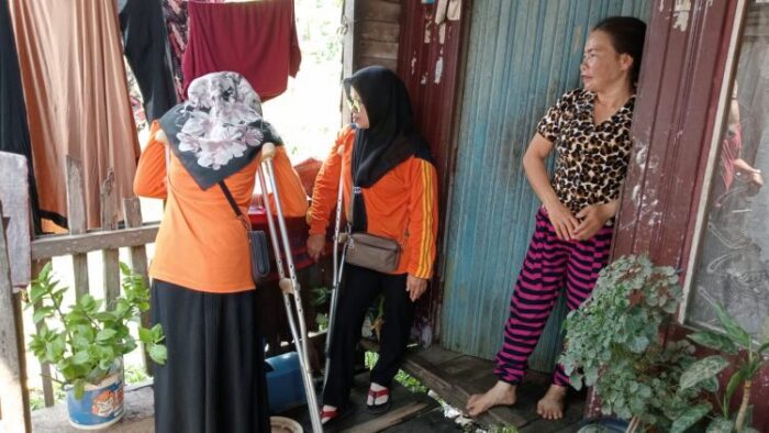 Two Diffability Liaison Officers wearing orange tops with crutches under their arms at the door of someone's home.