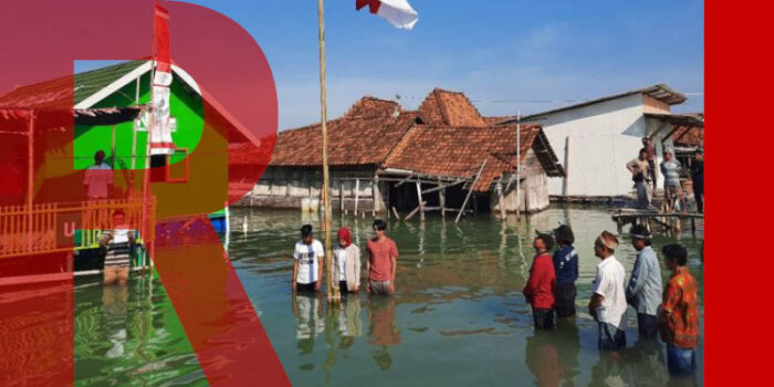 A group of people standing knee deep in floodwater in front of a flagpole with the Indonesian flag. Buildings in the background are flooded.