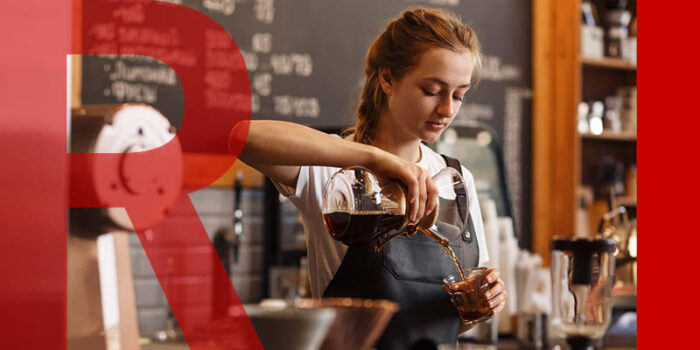 A young woman in an apron pouring filter coffee