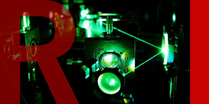 A dark room with machines and bright green lasers shooting between them