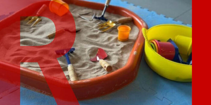 A sandpit with multicoloured tools such as trowels, rakes and buckets.