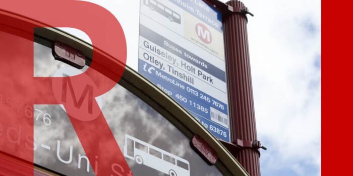  The roof of a bus stop with a sign over the top stating its destination.